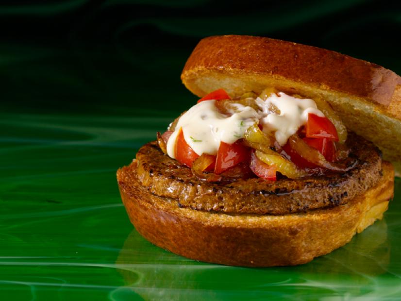 A veggie burger on thick slices of bread and topped with red peppers and white sauce
