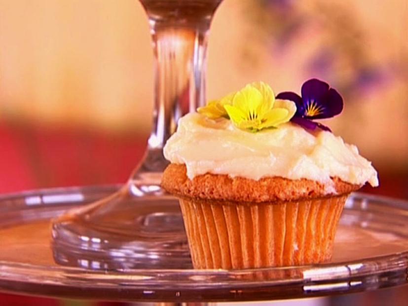 A yellow cupcake with light icing and a yellow and purple flower atop it