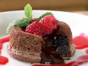A molten chocolate cake with raspberry sauce is topped with raspberries and mint.