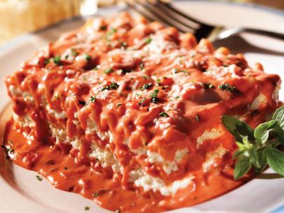 Lasagna in a puddle of tomato sauce while sprinkled and garnished with herbs 
