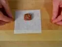A square piece of dark caramel sprinkled with salt is placed in the center of a square piece of wax paper.