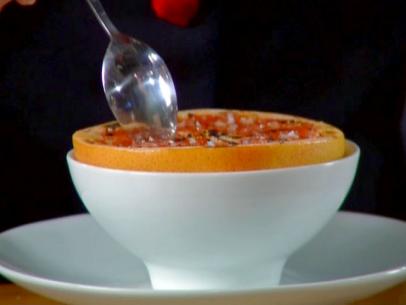 Grapefruit brulee is served in a white bowl on a white plate and topped with a sprinkle of salt.