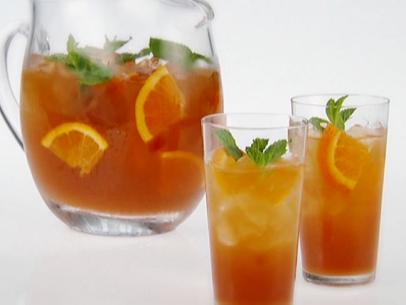 A pitcher and two glasses of orange ice tea is garnished with mint and quartered slices of orange.