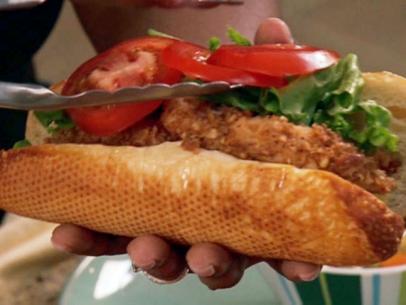 A pecan crusted catfish finger sandwich on a roll is topped with lettuce and sliced tomatoes.