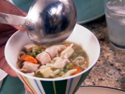 Mama Jeans chicken noodle soup with egg noodles, carrots, peas, celery and cubed skinless chicken breast is poured into a cup.