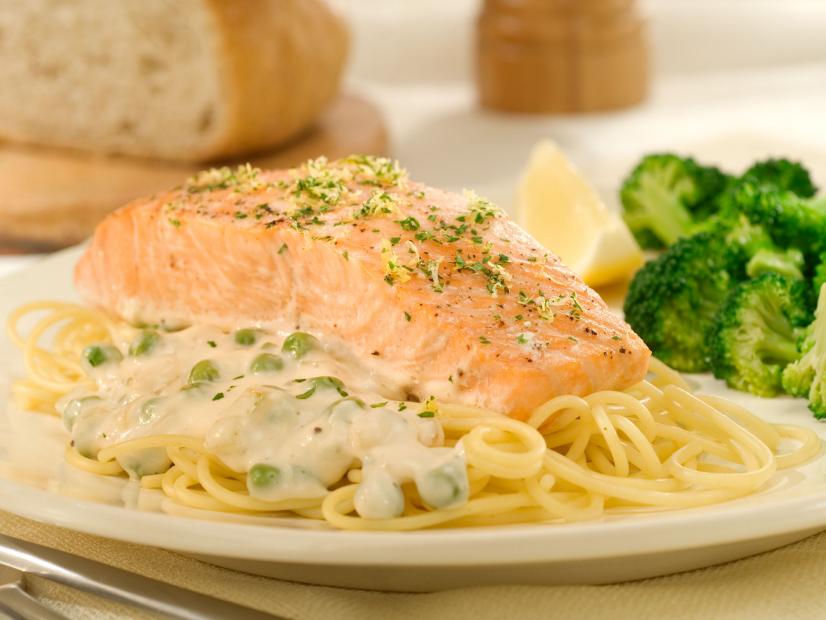 A piece of salmon sprinkled with herbs on a bed of pasta with creamy alfredo sauce