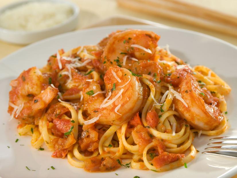 Shrimp on a bed of pasta with spicy tomato sauce on a small white plain dish