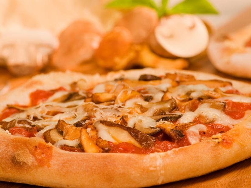 A pizza made with sliced wild mushrooms, tomato sauce and cheese placed on a wooden surface