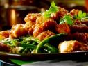 Sesame chicken over sauteed green beans is garnished with cilantro sprigs.
