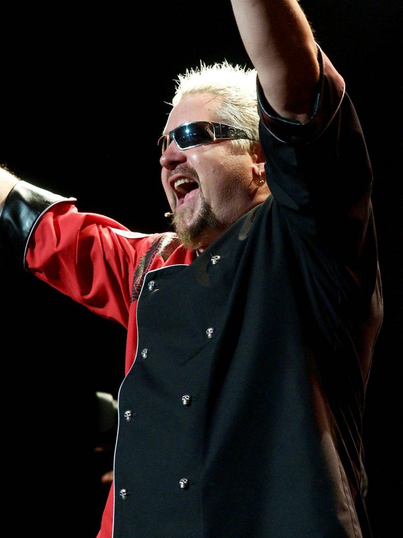 Guy Fieri on stage with hands raised and mouth wide open