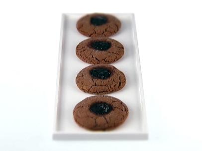 Four peanut butter cookies filled with blackberry jam aligned in a row on a plain white dish