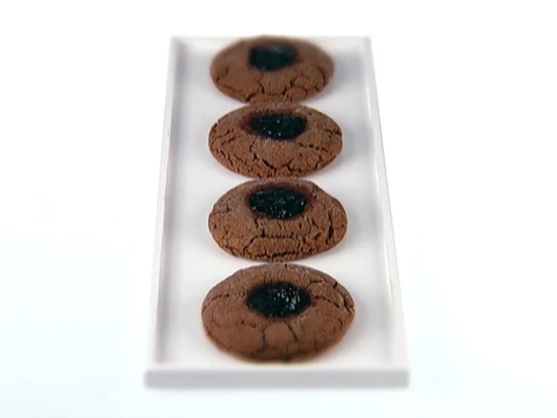 Four peanut butter cookies filled with blackberry jam aligned in a row on a plain white dish