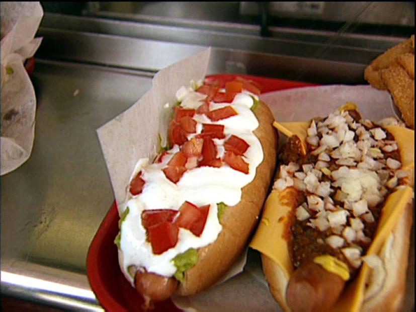 A hot dog topped with guacamole, sour cream and chopped tomatoes
