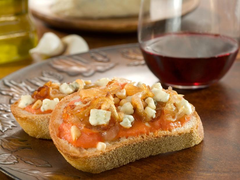 Bruschetta topped with caramelized onions and gorgonzola on a decorative wooden tray