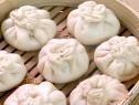 Pork steamed buns setting in a bamboo steamer are filled with a mixture of meat from spareribs, hoisin sauce, shredded cabbage, and thinly sliced scallions.