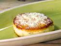 A hard polenta cake is topped with grated Parmigiano and served on a green platter.