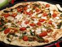 Chicken alfredo pizza is topped with red and yellow grape tomatoes, baby spinach, grated mozzarella, and parmesan.