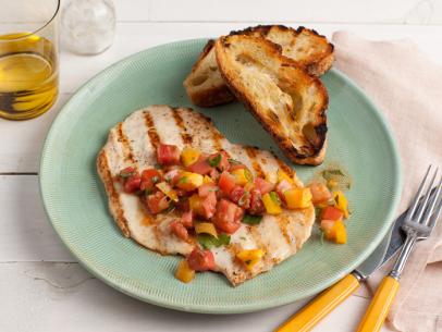 A thin slice of chicken topped with salsa on a plate alongside two pieces of toasted bread