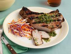 A sliced pork chop topped with a herb mixture and placed beside coleslaw