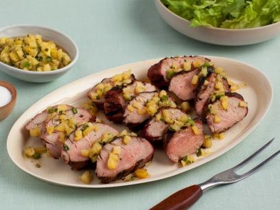 Pork tenderloin topped with a corn and herb mixture aligned in three rows on an oval plate