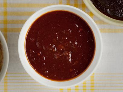 A Kansas City sauce in a small white bowl on top of a yellow and white plaid tablecloth