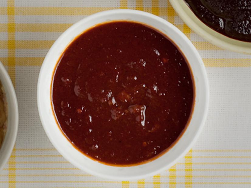 A Kansas City sauce in a small white bowl on top of a yellow and white plaid tablecloth