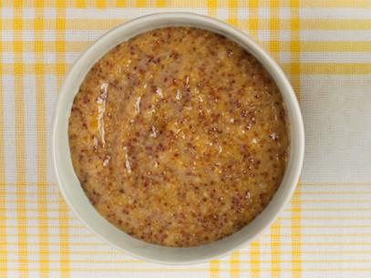 A peach mustard sauce in a small white dish on top of a yellow and white plaid tablecloth
