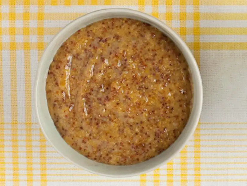 A peach mustard sauce in a small white dish on top of a yellow and white plaid tablecloth