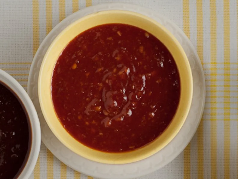 A sweet and sour sauce in a yellow bowl placed on a small white dish