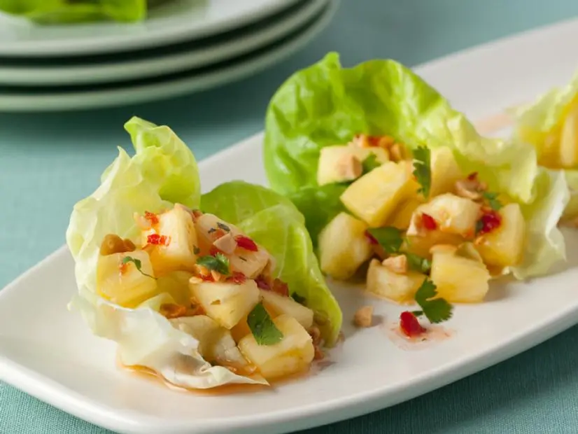 A close-up of a pineapple mixture on leaves of lettuce lying on a plain white platter