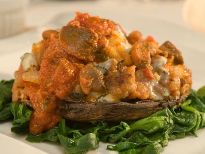 A sausage and gorgonzola  mixture on a portobello mushroom placed on a bed of greens
