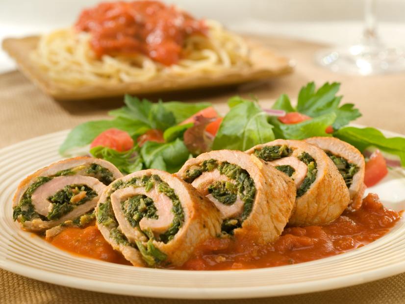 Spinach and cheese mixture rolled up into veal and cut into slices that are in a pool of tomato sauce