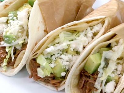 Carne asada tacos with green salsa is wrapped in brown paper.