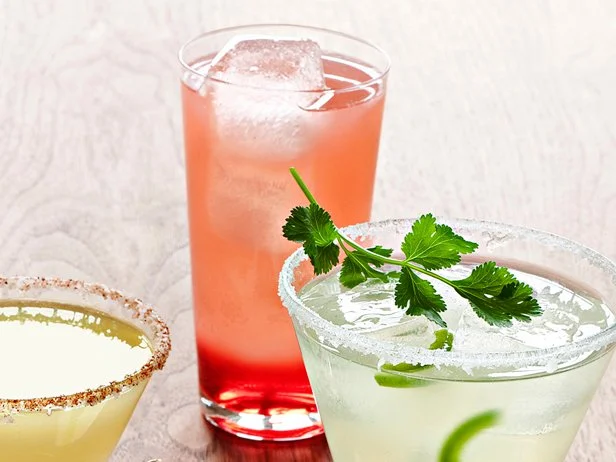A green, red and yellow colored margarita in various sized glasses placed on a wooden surface