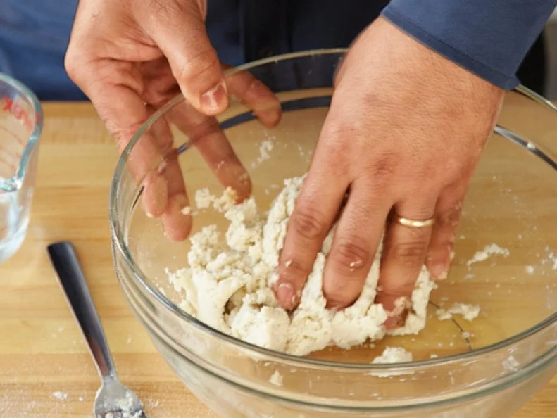 Hands mixing dough in a plain glass mixing bowl