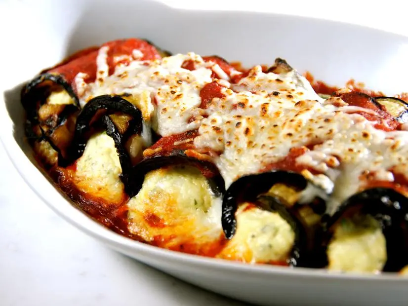 Cheese wrapped in a vegetable, aligned in a dish and covered with tomato sauce and cheese