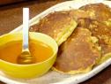 Corn cakes are served on a platter with a bowl of honey.