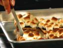Several small smores lying inside of a metal baking pan