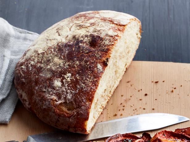 A round loaf of bread with a part of it missing that is placed on a cutting board along with a knife