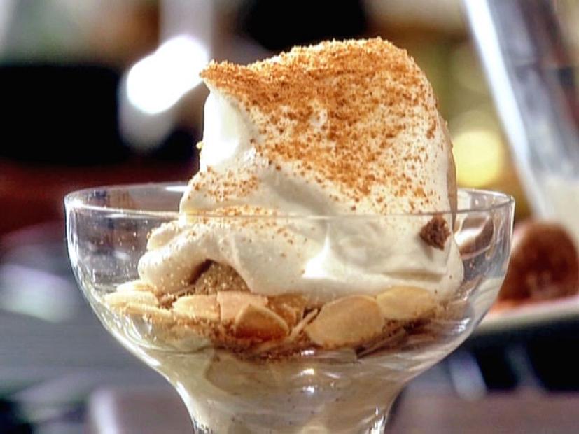 A clear glass containing gelato on sliced almonds and sprinkled with crushed cookies