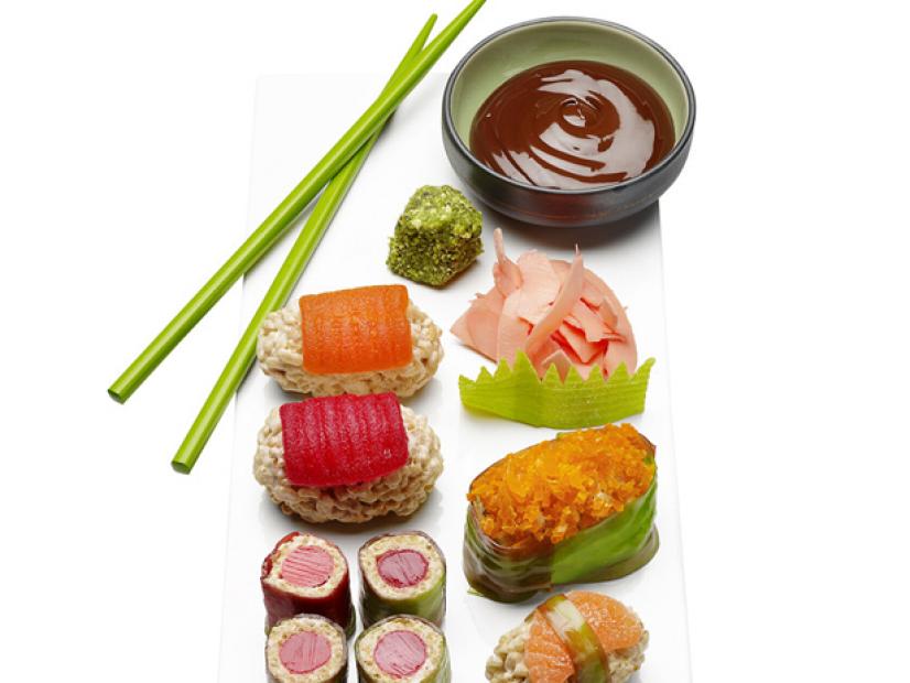 A variety of sushi with dipping sauce and green chopsticks against a white background