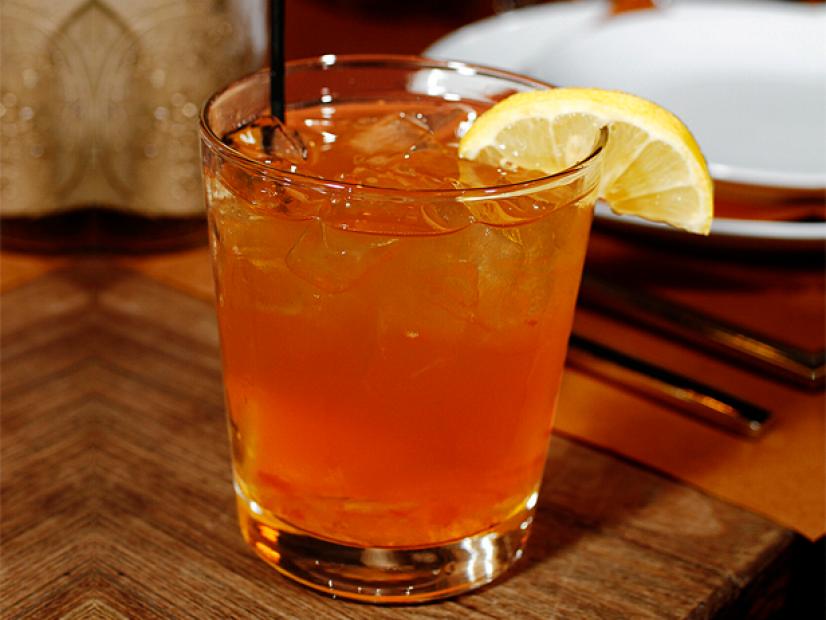 An orange colored cocktail garnished with a lemon wedge in a short class on a wooden table