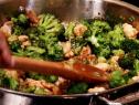 Neely's broccoli and chicken stir fry is mixed in a pan with a wooden spoon.