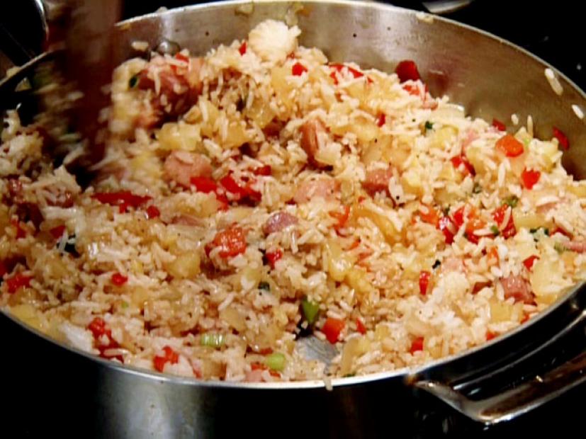 Neely's pineapple fried rice with chopped onion, green onion, red bell pepper, pineapple, and ham steak is mixed together in a skillet.