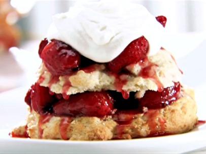 Alternating layers of shortcake and strawberries that are topped with cream and are placed on a plain white dish