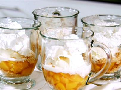 Four glass mugs filled with layers of chopped peaches, graham crackers and heavy cream