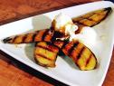 Grilled bananas spread out to resemble a star and topped with two scoops of ice cream drizzled with sauce