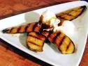 Grilled bananas spread out to resemble a star and topped with two scoops of ice cream drizzled with sauce