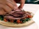 Chimichurri sauce, tomato relish, and sliced pieces of lamb are laid on top of a pita.
