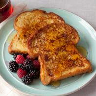 French Toast covered with syrup alongside a serving of raspberries and blackberries on a pale blue plate